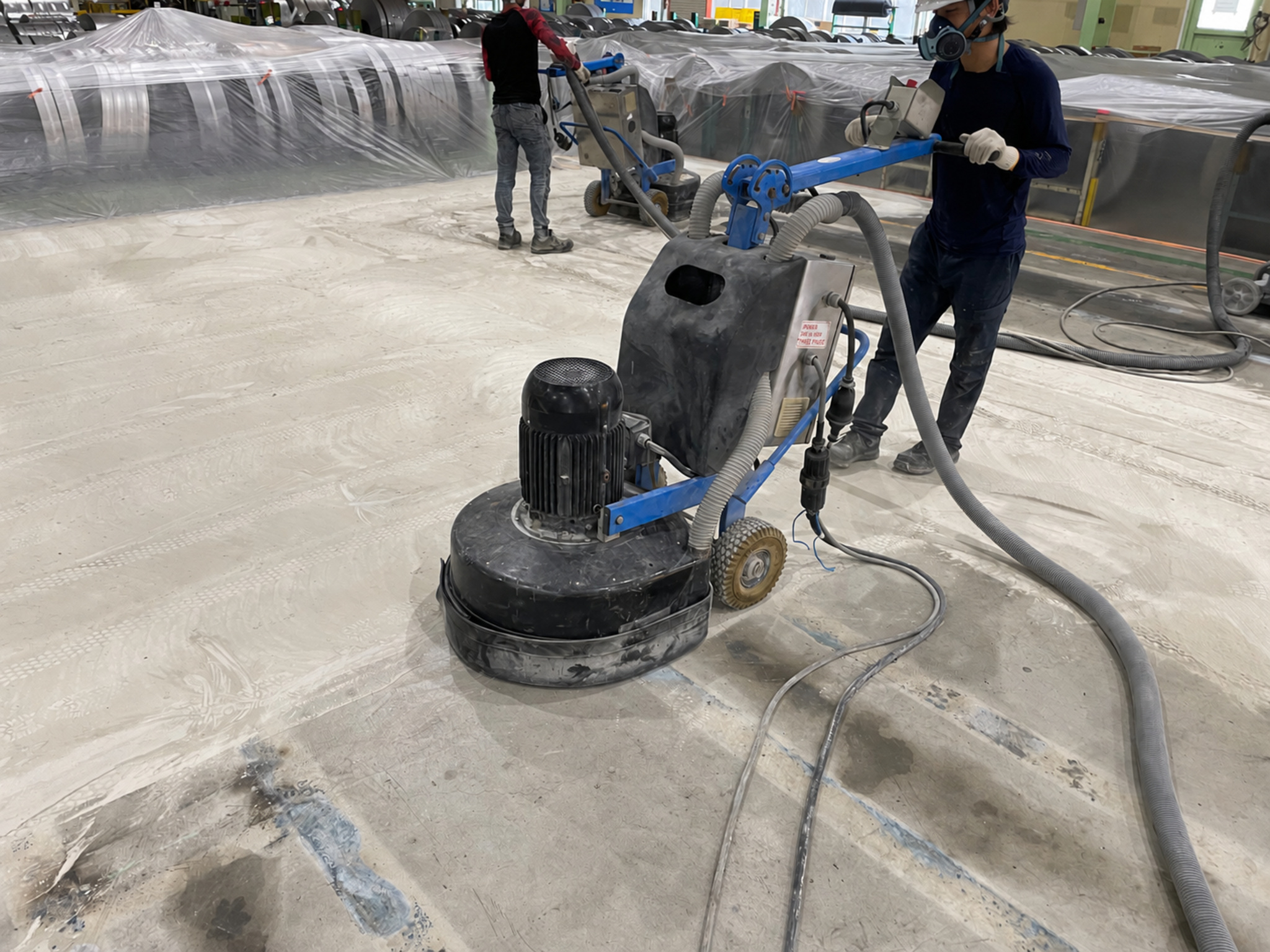 ホースを接続した床研磨機で下地を研磨する作業員